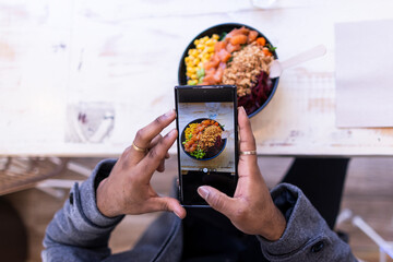 High angle view of black hands taking a photo of his healthy food. He has a poke bowl in front of...