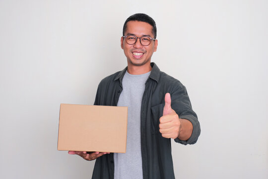 Adult Asian man smiling and give thumb up while holding a package box