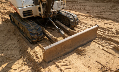 A mini excavator parked on brown dirt with closeup view of blade and tracks at a new home construction work site.