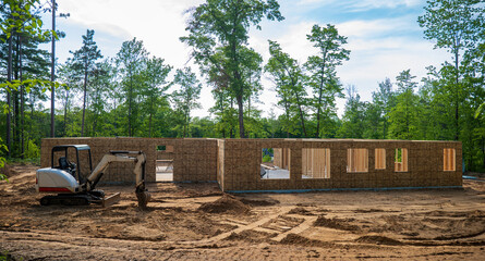 New home building project on a wooded building lot, with a mini excavator parked on the dirt at the construction site.