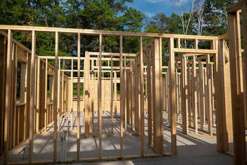 Closeup of wood framing studs of interior walls at new home construction work site in sunshine with shadows, with trees in the background.
