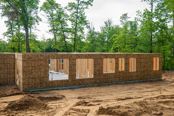 Fototapeta na wymiar New home building site in early construction stage, with plywood on exterior walls with window openings and wood framing studs inside, on a wooded lot.