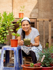Adult woman, surrounded by flowerpots and plants, looking and smiling ahead......
