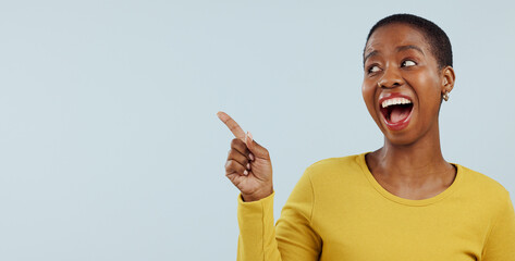 Happy black woman, pointing and surprise for advertising or marketing against a gray studio...