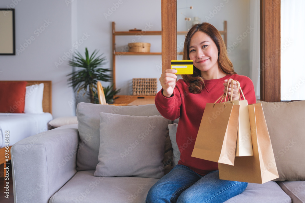 Wall mural Portrait image of a woman with shopping bags holding and showing a credit card for purchasing