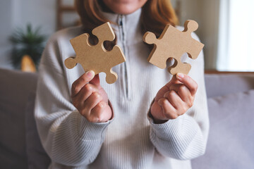 Closeup image of a woman holding and putting a piece of wooden jigsaw puzzle together