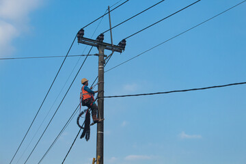 Electricity concept, Electricians Technician with hardhat and safety uniform checking repairing fixing electric wire on power pole. High voltage power lines and blue sky background.