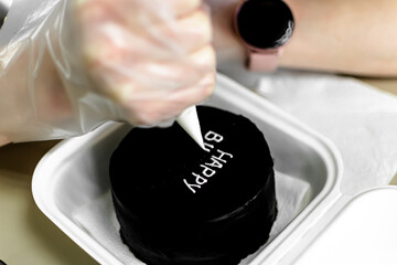 the pastry chef decorates a black cake. the inscription on the cake. Birthday