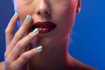 Caucasian woman wearing red lipstick and blue nail polish on blue background