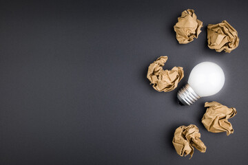 A small light bulb glowing in the group of crushed brown papers on black background, original idea,...