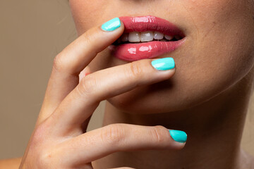 Caucasian woman wearing natural makeup and blue nail polish on beige background