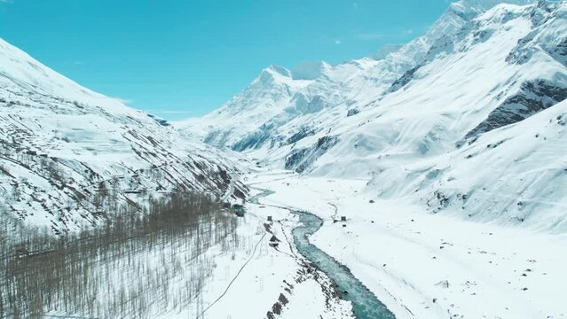 Forward Drone shot over snow clad mountains and extreme terrain of Indian Himalayas. Scenic aerial view of mountain valley with Chandra river at Sissu, India. Winters in Himalayas.