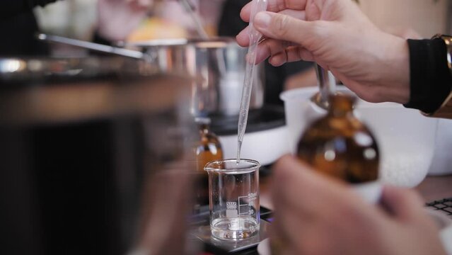 a woman's hand pours scented perfume into a glass flask, candle making workshop