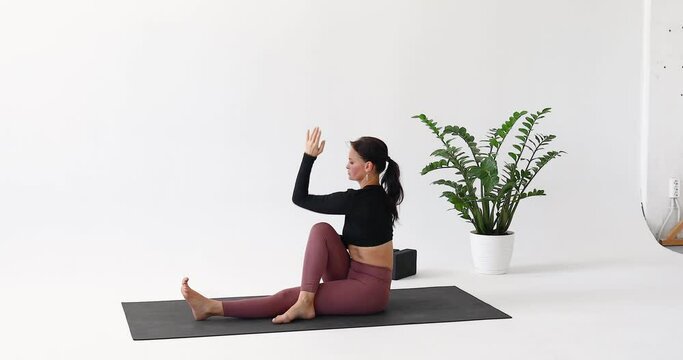 Athletic brunette woman practicing yoga, performing a variation of the Ardha Matsyendrasana exercise, half of the Lord of the Pisces pose, training in sportswear on a mat