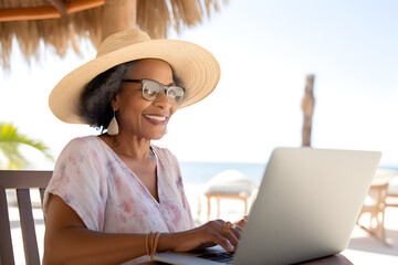 happy senior black woman working remotely on laptop on summer vacation - nomadic remote work concept