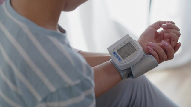 A little boy in the bedroom with a digital tonometer on his arm. A mother measures son pulse and blood pressure to monitor and check health indicators. A mom strokes her child back and supports him