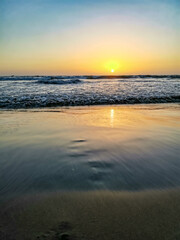 Sunset on Mandrem Beach in Goa, India. Bright and colorful sunset over the Indian Ocean, the Arabian Sea. A tropical beach with yellow sand and a bronze sunset.