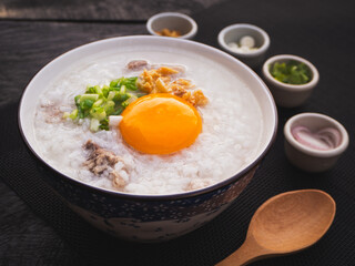 Rice soup or boiled rice with pork ribs and egg in bowl on wooden table background. Thai Food