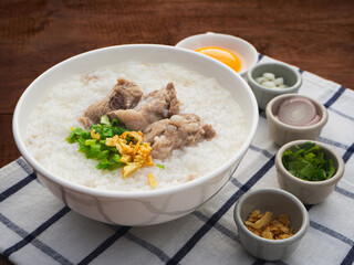 Rice soup or boiled rice with pork ribs in bowl on wooden table background. Thai Food