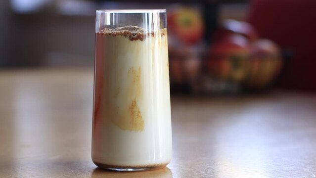 Homemade Coffee Frappe Bliss: A Step-by-Step Visual Guide. Mixing spoon glasses with milk and coffee frappe on wooden table at home, preparing refreshing drink during summer.