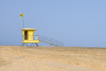 Yellow lifeguard tower on the beach with yellow beach safety flag in front of blue sky. Copy space.