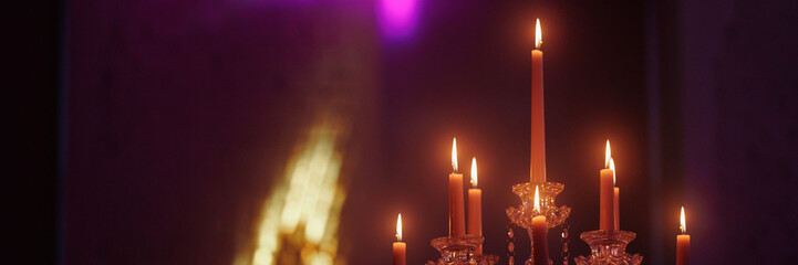 Candelabra with candles in a purple backlit background. Creepy or romantic atmosphere concept. Banner with copy space.