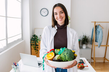 Portrait of young nutritionist woman holding a bowl of natural and organic fruits and vegetables...