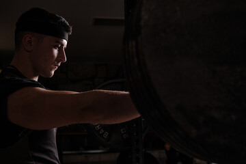 Strong young man lifting barbell while working out in gym