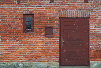 Red brick wall with small window and wooden doors. Background.