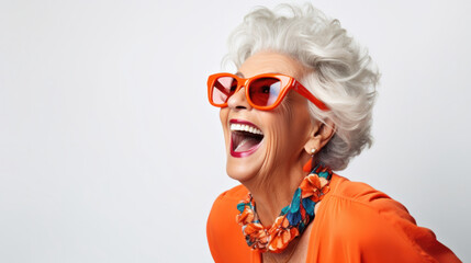 Vibrant senior woman laughing joyously in orange attire and statement sunglasses, embodying spirited elegance and positivity on a light background