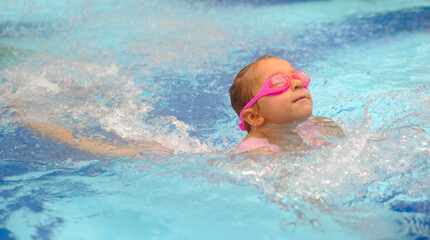 Child diving in swimming pool. Toddler kid jumping into the water in goggles learning to swim. Girl having fun in water, splashing in aquapark