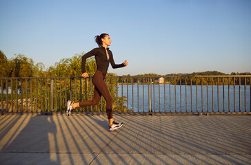 Woman who lives in a modern city is doing an active jogging workout in the morning. Side profile...