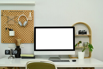 Modern workplace with blank computer monitor, books, headphone and houseplants on white table