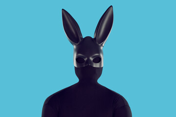 Studio shot of man disguised in black rabbit costume. Male model in faceless skintight monochromatic bodysuit and kinky long eared bunny mask standing like black silhouette isolated on blue background - obrazy, fototapety, plakaty