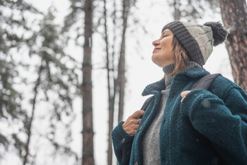 A young mature woman breathes fresh air and enjoys the snowfall in the winter forest. Winter walks...