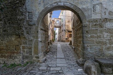 View through an arched gateway along a cobbled street into an ancient village without people