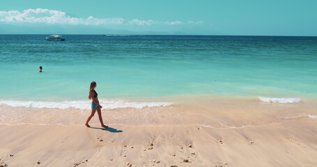Young woman taking a peaceful stroll along a serene tropical beach. Girl walking white sand,...
