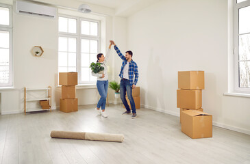 Happy couple dancing in their home on moving day. Excited spouses homeowners having fun in modern...