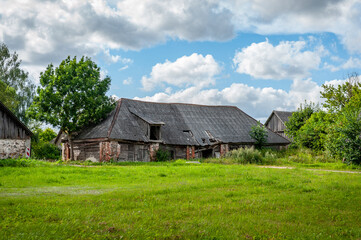 View on abandoned farm. Rural Latvian landscape with field, buildings, blue sky and clouds in sunny day.