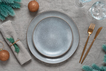 Christmas minimal table setting. Empty gray plates, gold cutlery, glasses and Christmas...