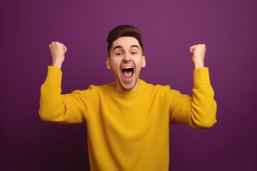 Fototapeta premium A young bearded man standing against a yellow background rejoicing in success and victory, clenching his fists in joy and happy to achieve his goal and tasks. Positive emotions. generative AI