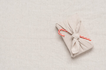 Christmas gift wrapped in fabric with red Christmas candy canes. Top view, flat lay. A traditional furoshiki gift.