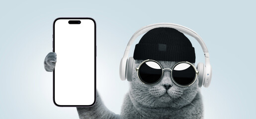 Funny hipster cat with fashion sunglasses and headphones shows a smartphone with a mockup display,...