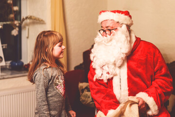 Little toddler girl talking to Santa Claus called Nikolaus or Weihnachtsmann in German. Happy smiling kid waiting for gifts. Santa with golden book. Xmas, childhood, holiday