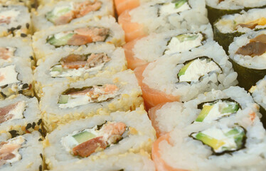 Close-up of a lot of sushi rolls with different fillings lie on a wooden surface. Macro shot of cooked classic Japanese food with a copy space.