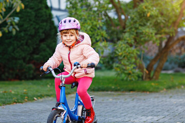 Little preschool girl riding bike. Kid on bicycle outdoors. Happy child enjoying bike ride on her way to school on warm summer day. Preschooler learning to balance on bicycle in safe helmet.