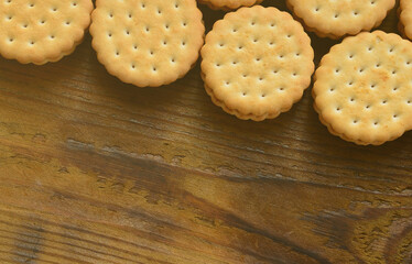 A round sandwich cookie with coconut filling lies in large quantities on a brown wooden surface. Photo of edible treats on a wooden background with copy space