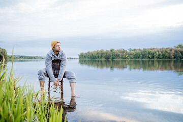 A man is sitting in the water on an old chair and looking at the lake, a guy is admiring the...