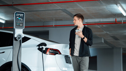 Young man travel with EV electric car to shopping center parking lot charging in downtown city...