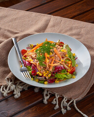 A plate of tuna salad with carrots and tomatoes on a wooden floor